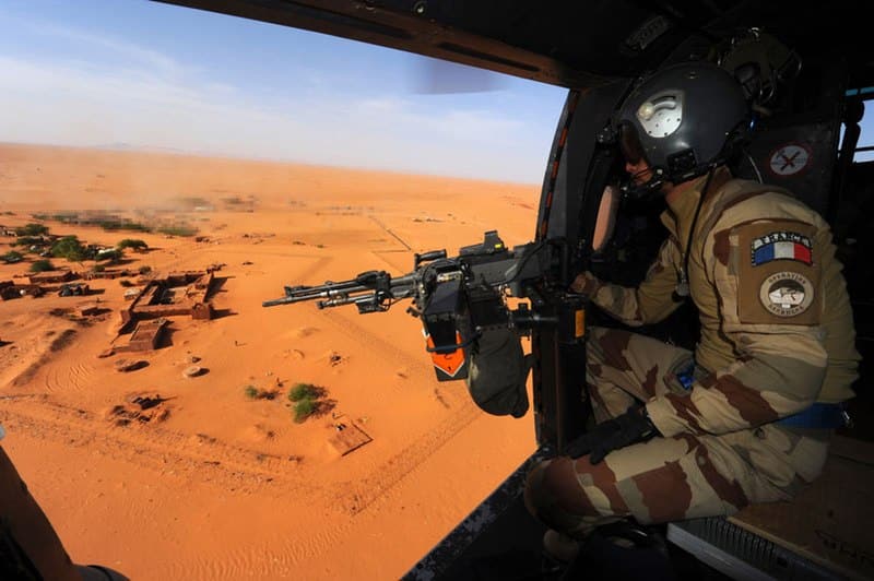 Soldat dans un hélicoptère survolant le désert.