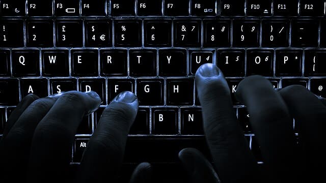 Des mains qui tapent sur un clavier d'ordinateur. Ambiance sombre.